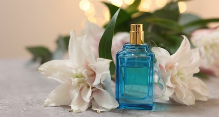 Bottle of perfume and beautiful lily flowers on table against beige background with blurred lights, closeup