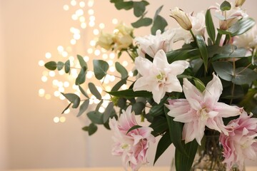 Bouquet of beautiful lily flowers against beige background with blurred lights, closeup