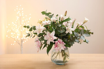 Bouquet of beautiful lily flowers in vase on wooden table against beige background