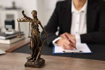 Notary with clipboard writing notes at workplace in office, focus on statue of Lady Justice