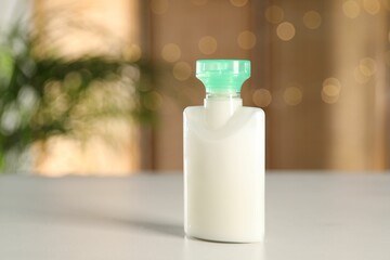 Mini bottle of cosmetic product on white table against blurred background. Space for text