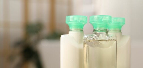 Mini bottles of cosmetic products on blurred background, closeup. Space for text