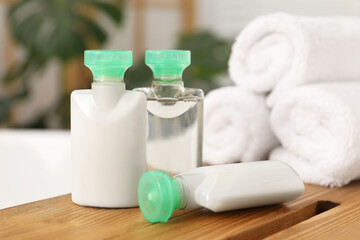Wooden tray with mini bottles of cosmetic products and rolled towels on bath tub in bathroom, closeup