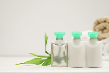 Mini bottles of cosmetic products and green branch on white table. Space for text