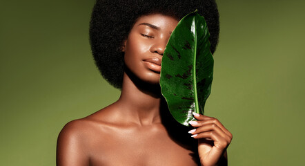 Organic natural cosmetics concept.  Beauty portrait of young beautiful african american woman with posing with banana leaf curly hair against green exotixc plants background.