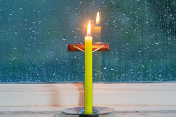 Crucifix with lit candle in front of the rainy window. Faith and meditation scenario