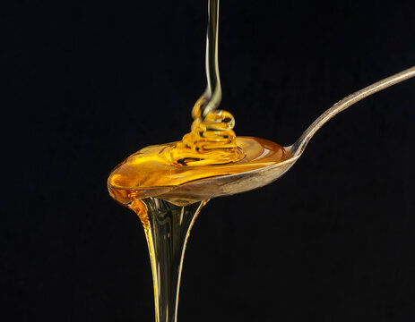Honey falling on a spoon isolated on black background.
