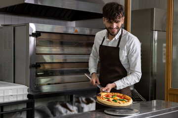 Smiling cooker preparing tasty pizza in pizzeria