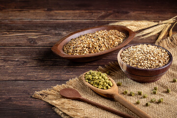 Barley in wooden bowl and granulated hops in a wooden spoon on a wooden table. Ingredients for craft beer.