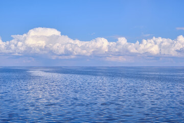 A tranquil seascape with gentle ripples on the water and billowy white clouds in the sky, their reflections dancing on the serene surface