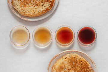 Different classes of maple syrups in different colours in glass bowls with pancakes next to them