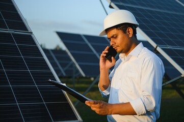 An Indian male engineer working on a field of solar panels. The concept of renewable energy