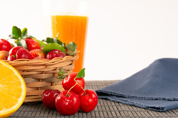 Fresh acerola juice in a glass cup in a bamboo place mat with sliced oranges and acerola fruits front view