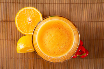 Fresh acerola juice in a glass cup in a bamboo place mat with sliced oranges and acerola fruits top view