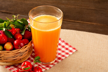 Fresh acerola juice in a glass cup in a bamboo place mat with sliced oranges and acerola fruits front view