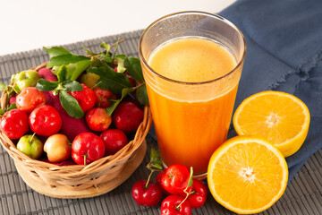 Fresh acerola juice in a glass cup in a bamboo place mat with sliced oranges and acerola fruits top view