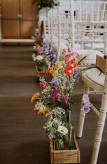 Close up of colourful flowers and chiavari chairs ready for a wedding ceremony looking up the aisle