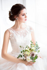 Naklejka premium Beautiful brunette woman with bouquet posing in a wedding dress