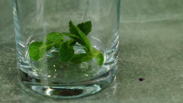Piece of mint falls in glass on table closeup. Natural components destined for cocktail promising delightful and refreshing experience
