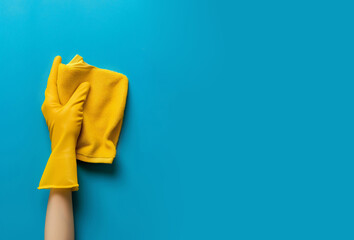 A woman's hand in a yellow glove holds a yellow cleaning rag on a blue background. Photo concept of spring cleaning in the office and home. Design banner template with place for text