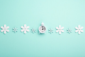 White Alarm Clock and Spring Daisy Flowers on Pastel Blue Mint Background. Springtime Concept.