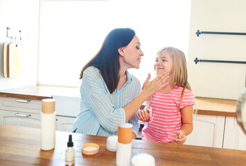 Cute smiling mother and daughter applying face cream