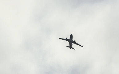 airplane flying through clouds (seen from below in dark silhouette against bright blue sky) shadow, outline of commercial airline plane seen from the ground