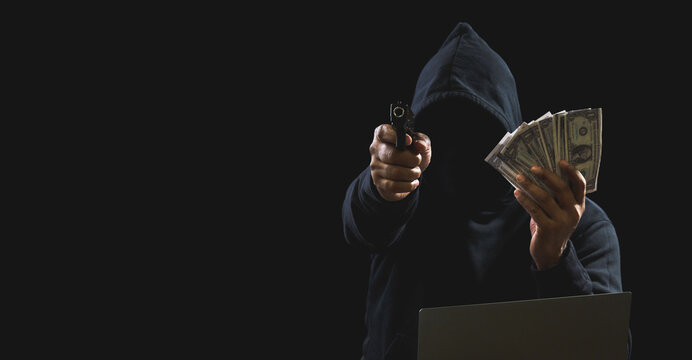 Portrait killer hacker gangster spy man one person in black hoodie standing look hand holding gun money dollar obtained from robbery threats crime attack victim people night dark background copy space