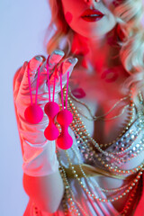 Beautiful blonde woman in a white sexy dress and white gloves holds pink Kegel balls and Ben Wa balls in her hand. Traces of kisses on the body and face. Blue pink background. Sex toys Geisha balls