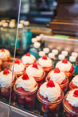 Cups of strawberries topped with whipped cream and a berry garnish on a cafe counter.