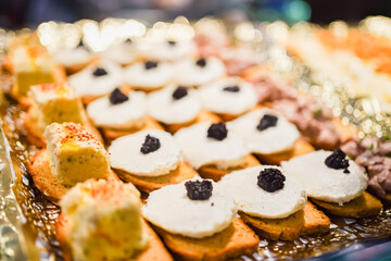 Gourmet canapes topped with white cheese and black caviar on a golden platter.