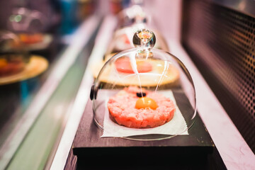 Steak tartare under a glass cloche, presented on a wooden board.