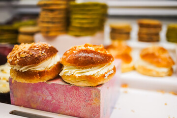 Fresh cream-filled buns sprinkled with nuts, displayed in a pastry shop.