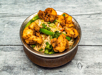 gobi noodle or fried cauliflower noodles served in copper dish isolated on wooden table top view of indian spicy food
