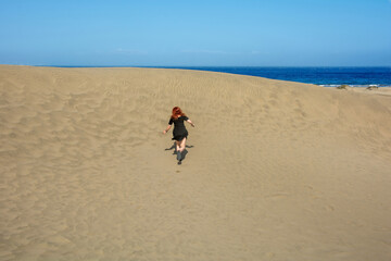 Young woman running up a sand dune