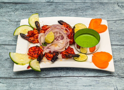 Saffron grilled prawn or tandoori jhinga with lemon and onion served in dish isolated on wooden table top view of indian spicy food