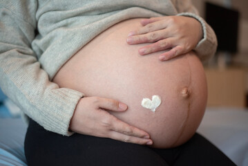 Close up of pregnant woman with lotion heart shaped  on her belly symbolising love. Health and appearance care tummy skin moistening and nourishment concept.