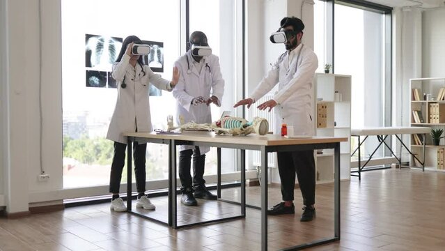 Science, technology, virtual reality and people concept. Group of multiethnic medical students or workers using virtual reality goggles to exam human skeleton lying on the table.