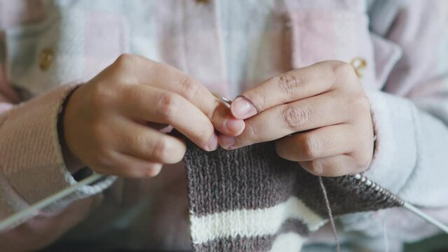 Female caucasian hands knitting brown wool scarf with knitting needles.