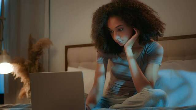 Night dark bedroom African American woman looking at computer screen search on laptop device female businesswoman working deadline girl buying online choosing movie sleepless evening insomnia at home