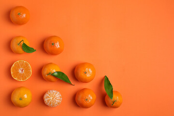Delicious tangerines and green leaves on orange background, flat lay. Space for text