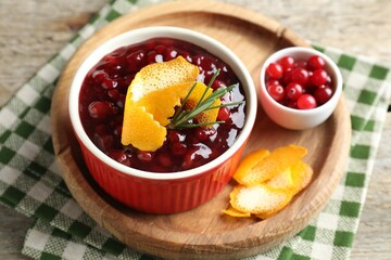 Cranberry sauce in bowl, fresh berries, rosemary and orange peels on table, closeup