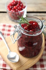 Fresh cranberry sauce in glass jar, rosemary and spoon on table