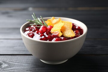 Fresh cranberry sauce, rosemary and orange peel in bowl on black wooden table, closeup