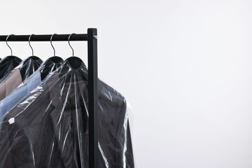 Dry-cleaning service. Many different clothes in plastic bags hanging on rack against white...