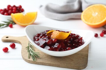 Fresh cranberry sauce with orange peel in bowl and rosemary on white wooden table, closeup