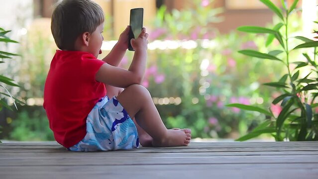 Little cute boy sits on the porch of the house and takes a pictures with mobile phone