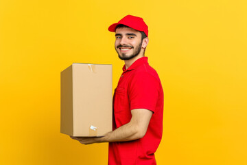 Full body side view happy delivery guy employee man in red cap T-shirt uniform workwear work as dealer courier hold cardboard box isolated on plain yellow background studio portrait.