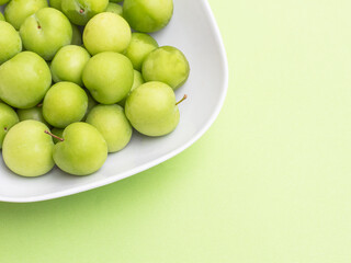 group of green plums in white bowl on green background. fresh  green plum