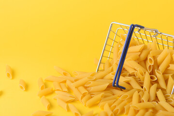 Pasta in shopping basket on yellow background.
